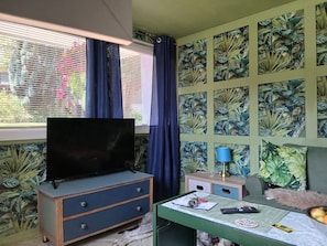A room with a television on a dresser, a desk with a lamp, and a wall with a tropical leaf pattern. - Dumfries 2BR Apartment Free Parking Near Robert Burns Centre (Dumfries)
