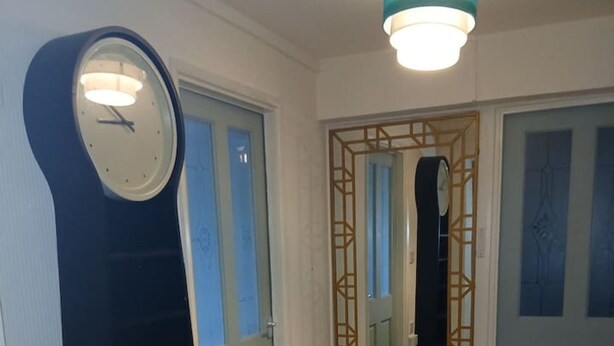 Un pasillo con un reloj de pared grande, un espejo y un pequeño banco.