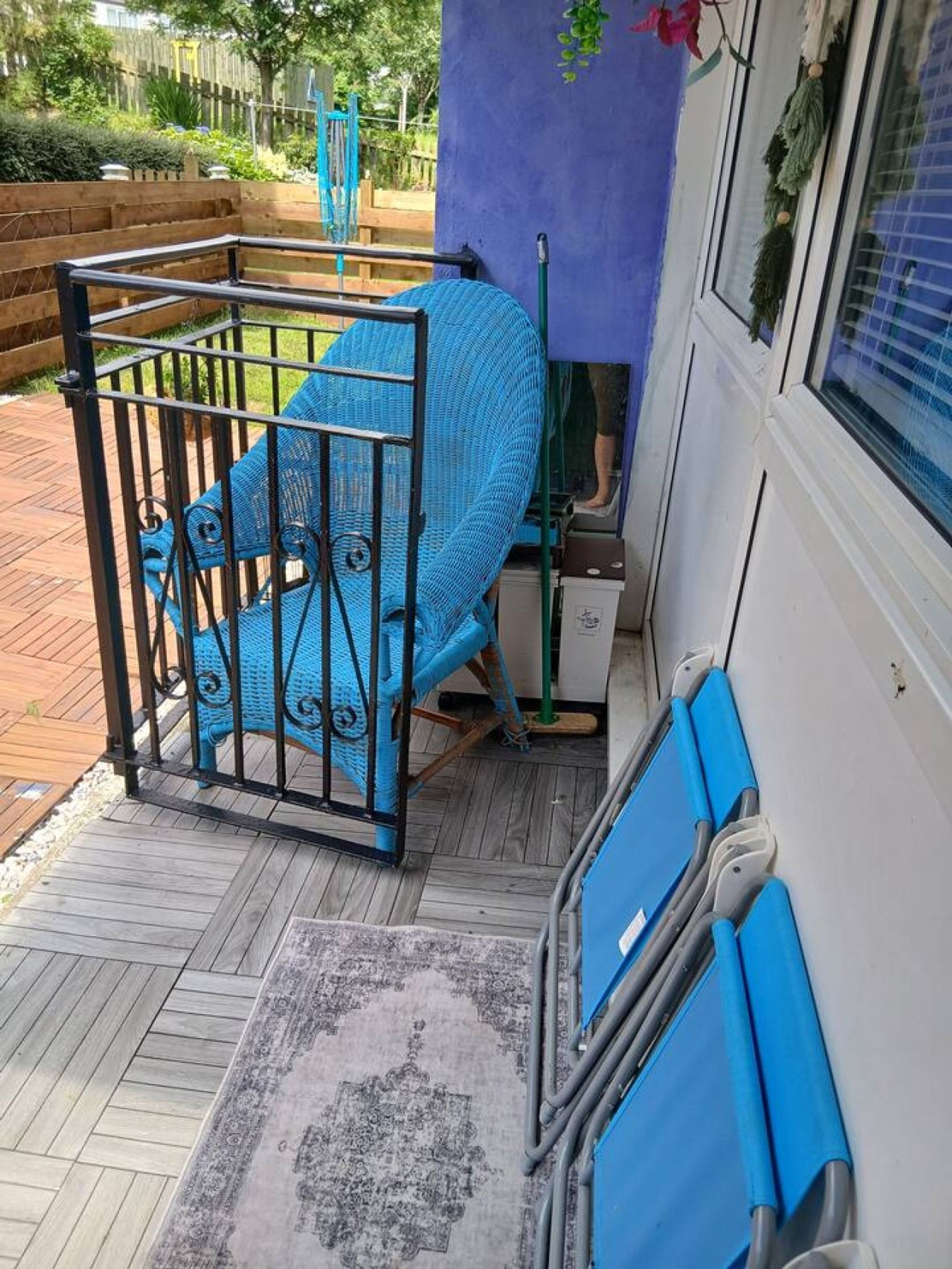Una silla azul con estructura metálica, un banco azul y un tapete estampado sobre una terraza de madera.
