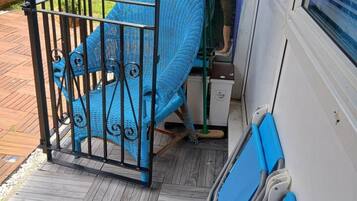 Una silla azul con estructura metálica, un banco azul y un tapete estampado sobre una terraza de madera.