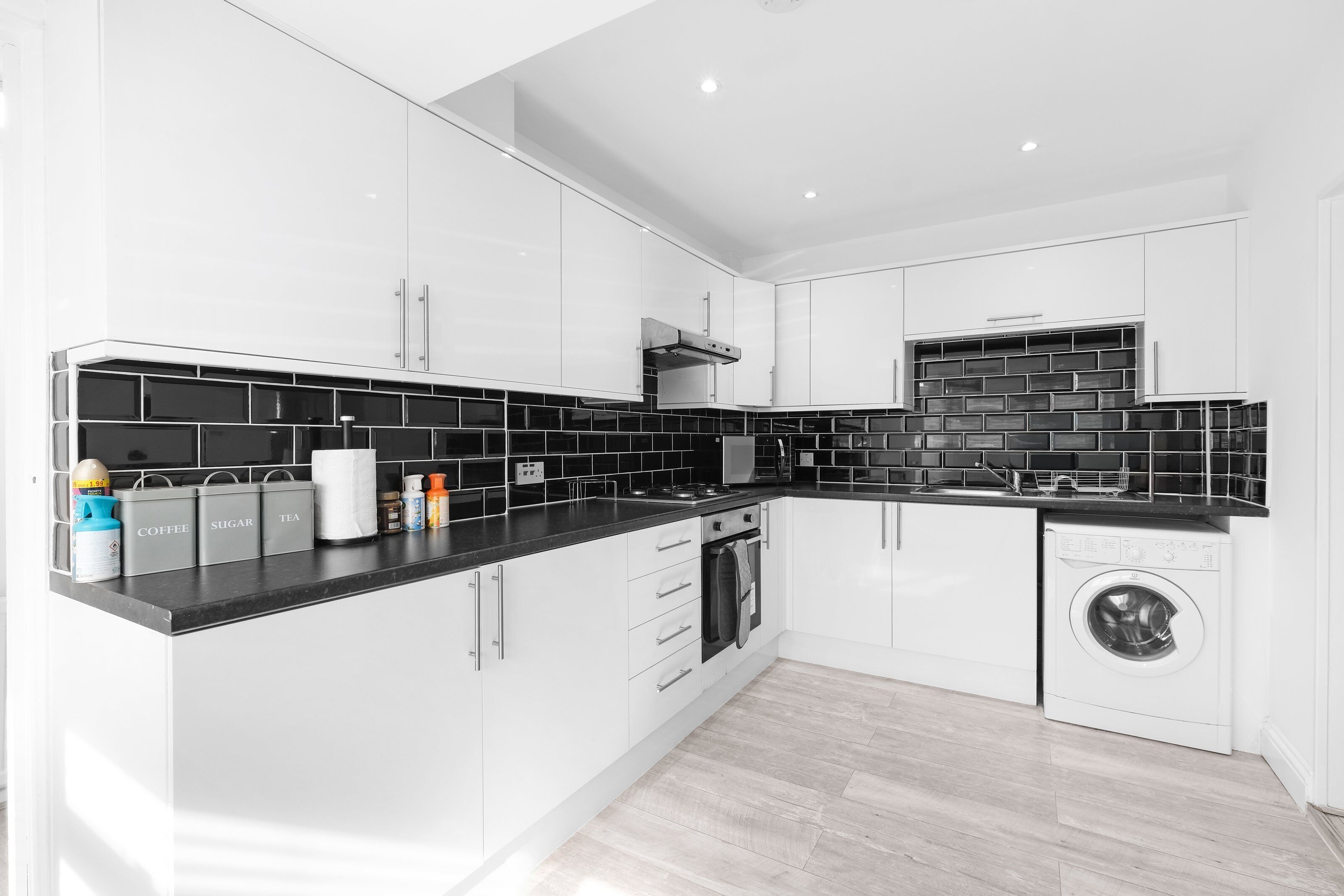 A modern kitchen with white cabinets, black backsplash, and a built-in washing machine.