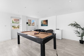 A modern living room with a pool table, a sofa, a coffee table, and a potted plant. - 8-Bed Detached House with Games Room | Cheshunt (Waltham Cross)