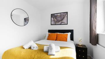 A hotel room with a bed, a round mirror, a painting, and a nightstand.