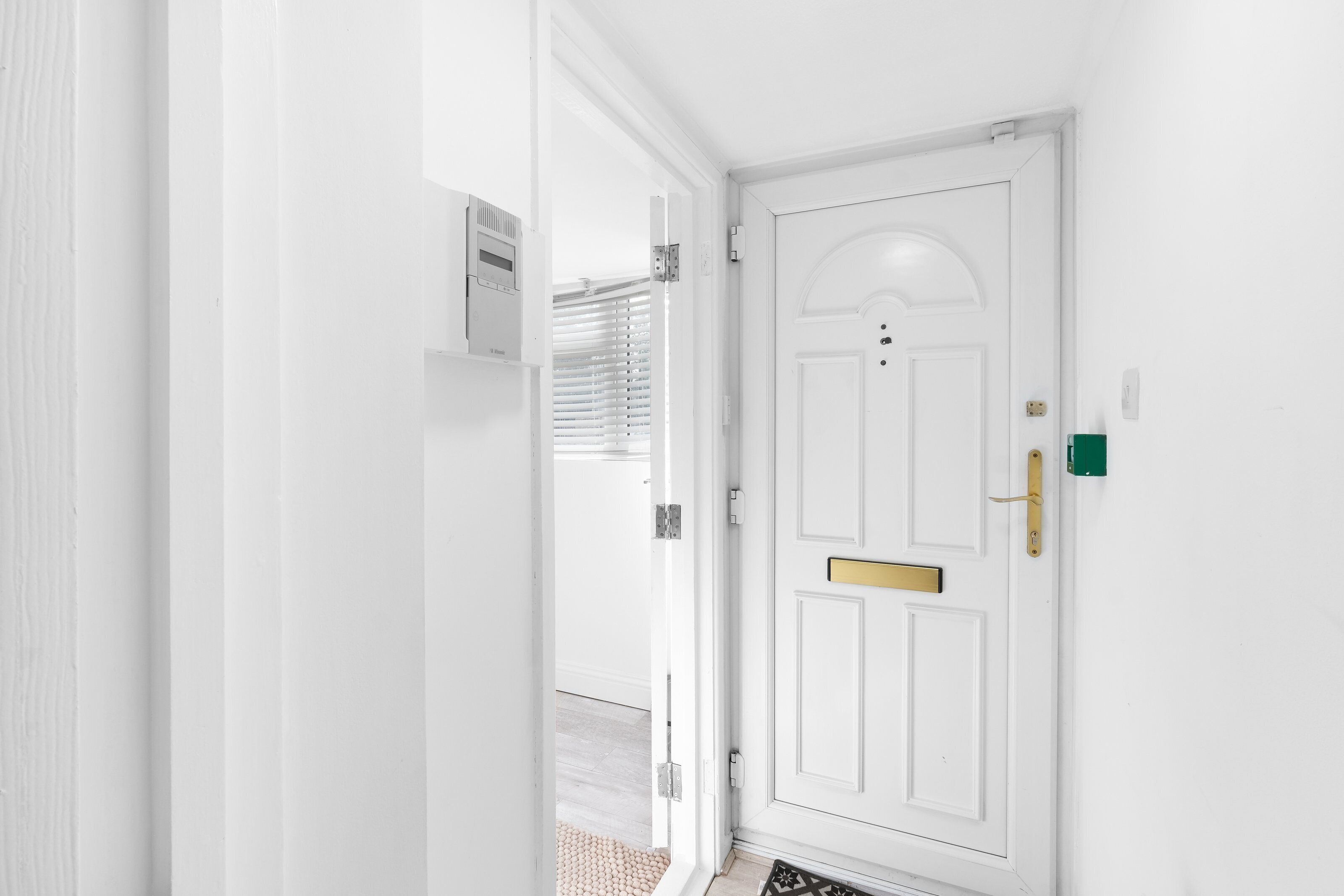 A white door with a brass handle and a mail slot, leading to a room with a light-colored floor and a small rug.
