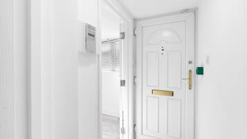 A white door with a brass handle and a mail slot, leading to a room with a light-colored floor and a small rug.