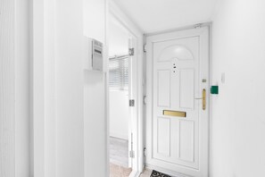 A white door with a brass handle and a mail slot, leading to a room with a light-colored floor and a small rug. - 8-Bed Detached House with Games Room | Cheshunt (Waltham Cross)