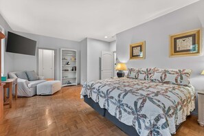 A bedroom with a bed, a side table, a lamp, a wardrobe, a TV, and a shelf with books and decorative items.