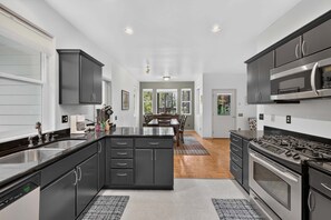 A modern kitchen with dark cabinetry, a central island, and a dining area with a view of the outdoors. - Creekside Inn- sleeps 6, pets ok-  perfect private getaway (McCall)