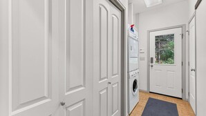 Un pasillo con una lavadora, una puerta con ventana y un tapete gris en el suelo.
