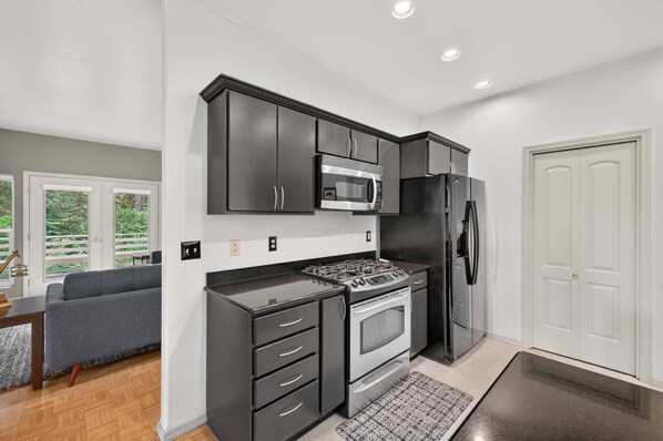 A modern kitchen with dark cabinetry, stainless steel appliances, and a view to the outdoors.