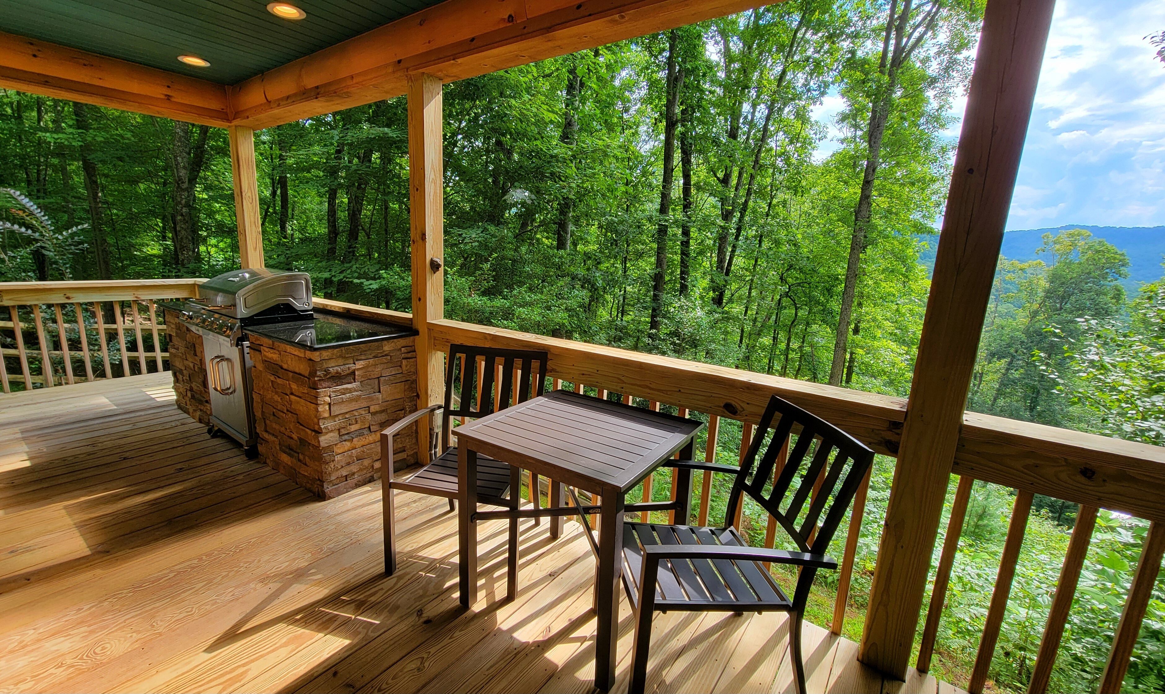 Een overdekt terras met een stenen barbecue, houten stoelen en een tafel.