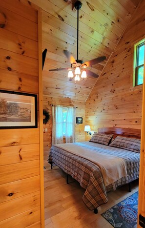 A cozy wooden cabin bedroom with a bed, a ceiling fan, and a framed picture on the wall. - Fernwood Hollow- Romantic One Bedroom in Bryson City NC (Bryson City)