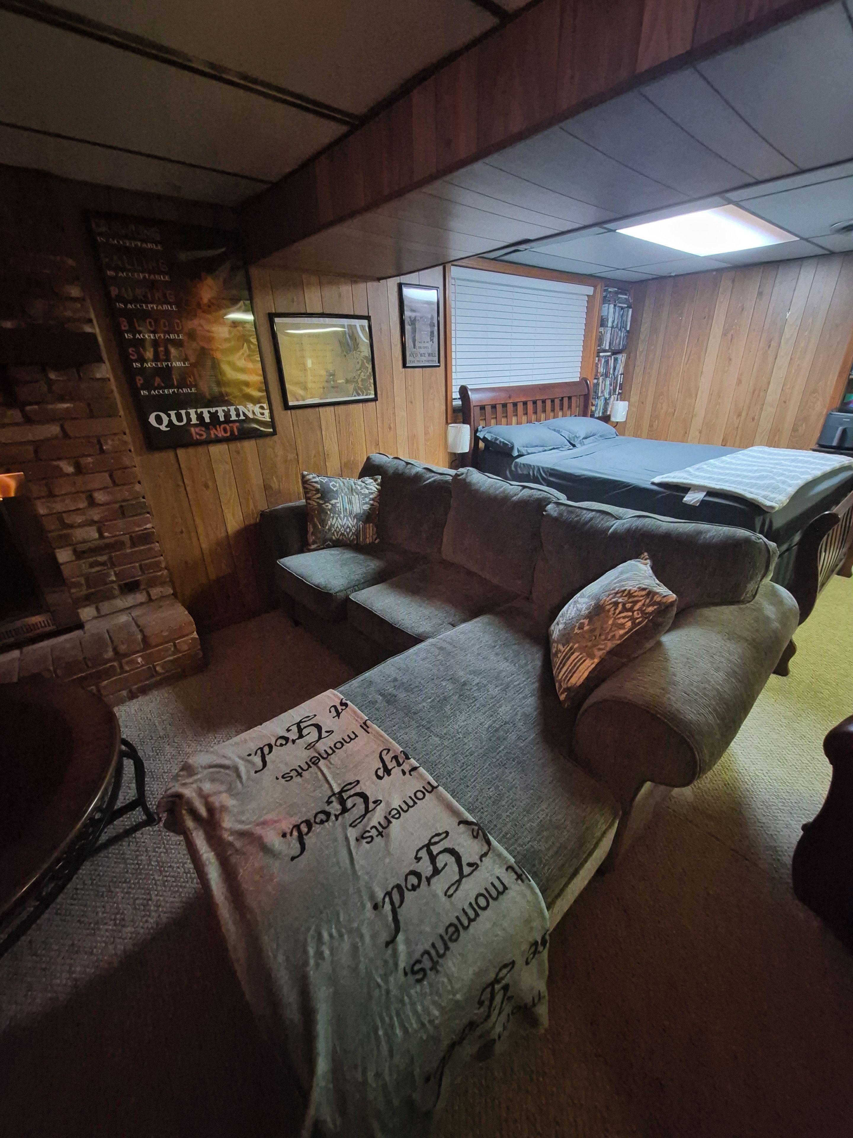 A room with a wooden ceiling, a sofa, a bed, a fireplace, and a wall with motivational quotes.