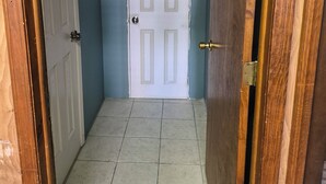 A hallway with a white door, wooden doors on either side, and a tiled floor.