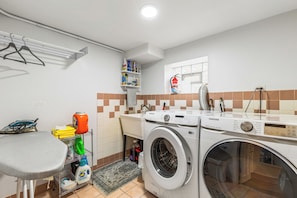 A laundry area with a Samsung washing machine, a drying rack, a shelf with cleaning supplies, and a small table.