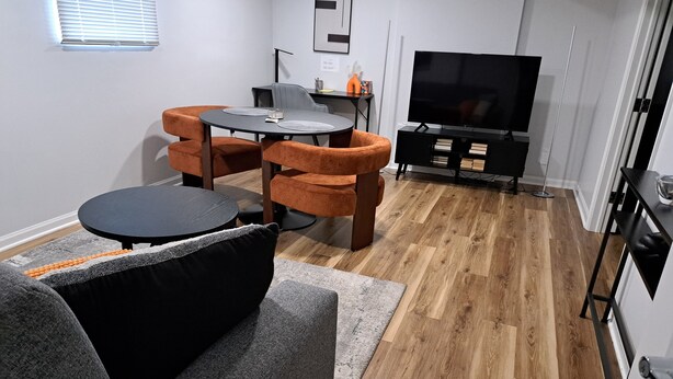 En moderne stue med sofa, rundt sofabord og spiseplads med bord og stole. Et fladskærms-TV er monteret på væggen.