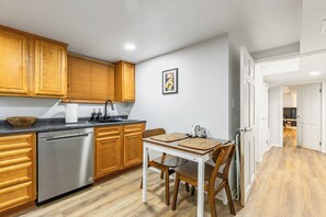 A modern kitchen with wooden cabinets, a stainless steel dishwasher, and a dining table with chairs.