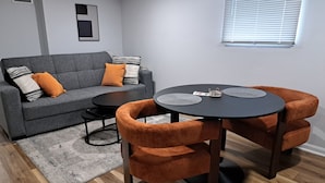En moderne stue med en grå sofa, orange lænestole, et rundt sort bord og en grå måtte.
