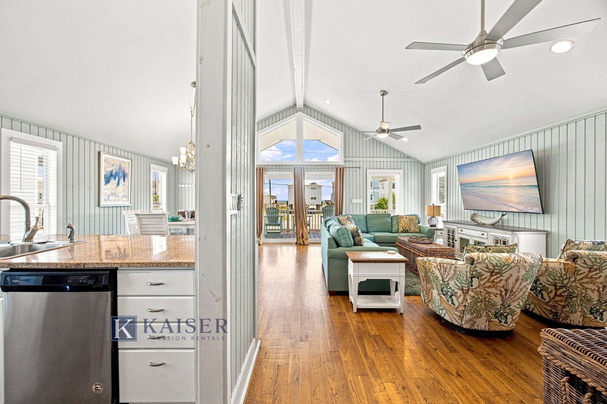 A spacious living area with a large television, a ceiling fan, and a view to the outside.