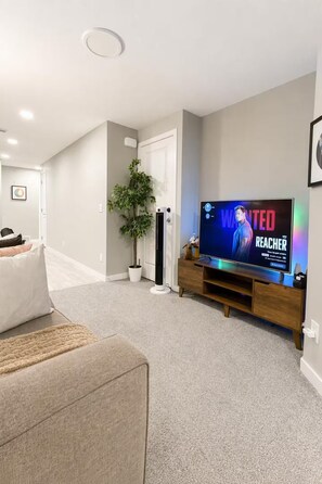A modern living room with a flat-screen TV, a potted plant, and a beige sofa. - Luxury 2‑bed walkout Suite near CalgaryYYC airport (Calgary)