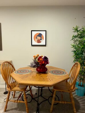 A round wooden table with two chairs, a vase with flowers, and a framed picture on the wall. - Luxury 2‑bed walkout Suite near CalgaryYYC airport (Calgary)