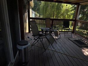 A covered outdoor deck with a table and chairs, a trash can, and a view of a green landscape. - Spacious 4-bedroom house in charming Oak Grove with AC (Oak Grove)