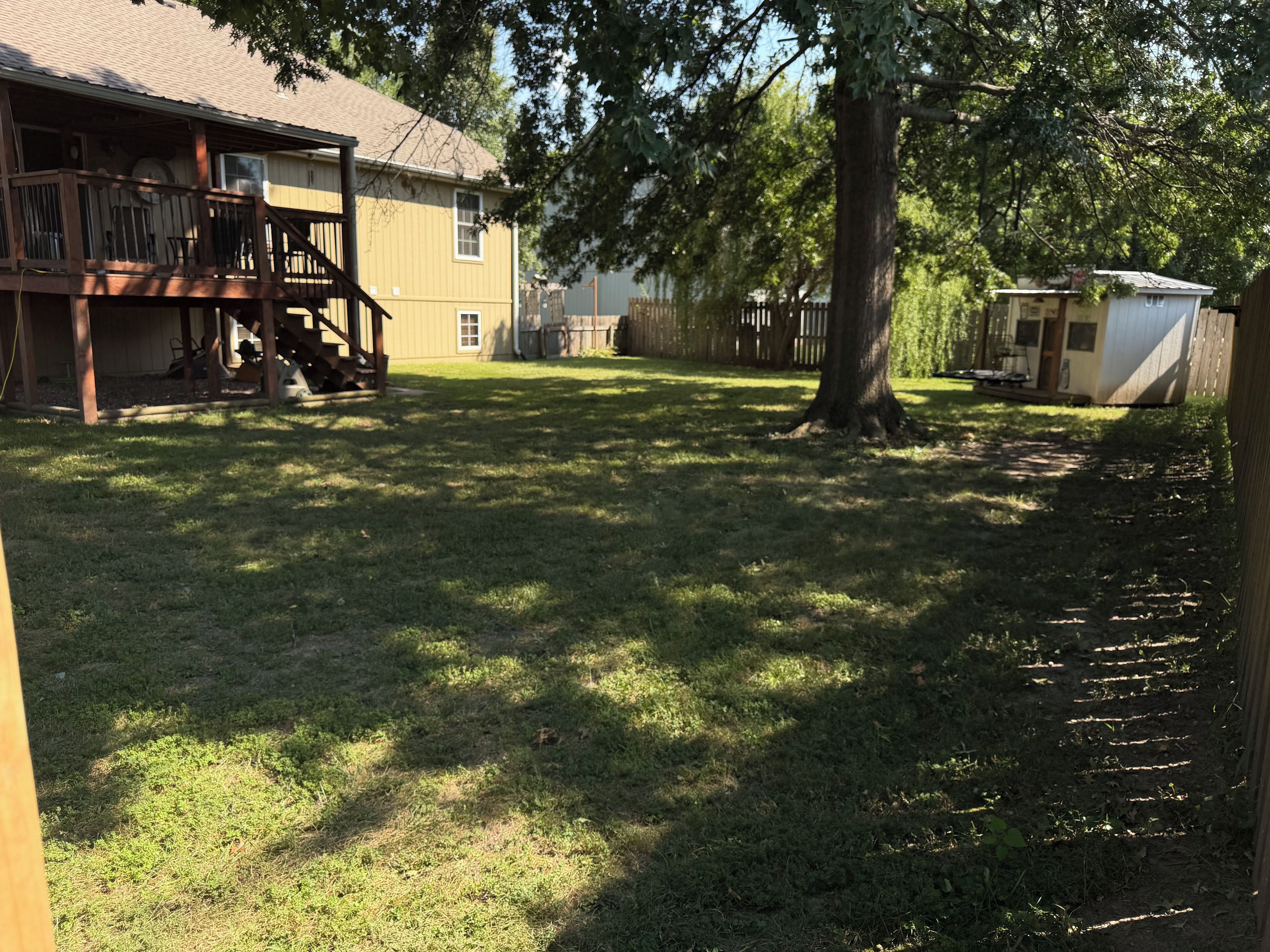 A residential backyard with a wooden deck, a covered patio, and a fenced area.