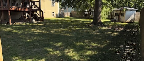 A residential backyard with a wooden deck, a covered patio, and a fenced area.