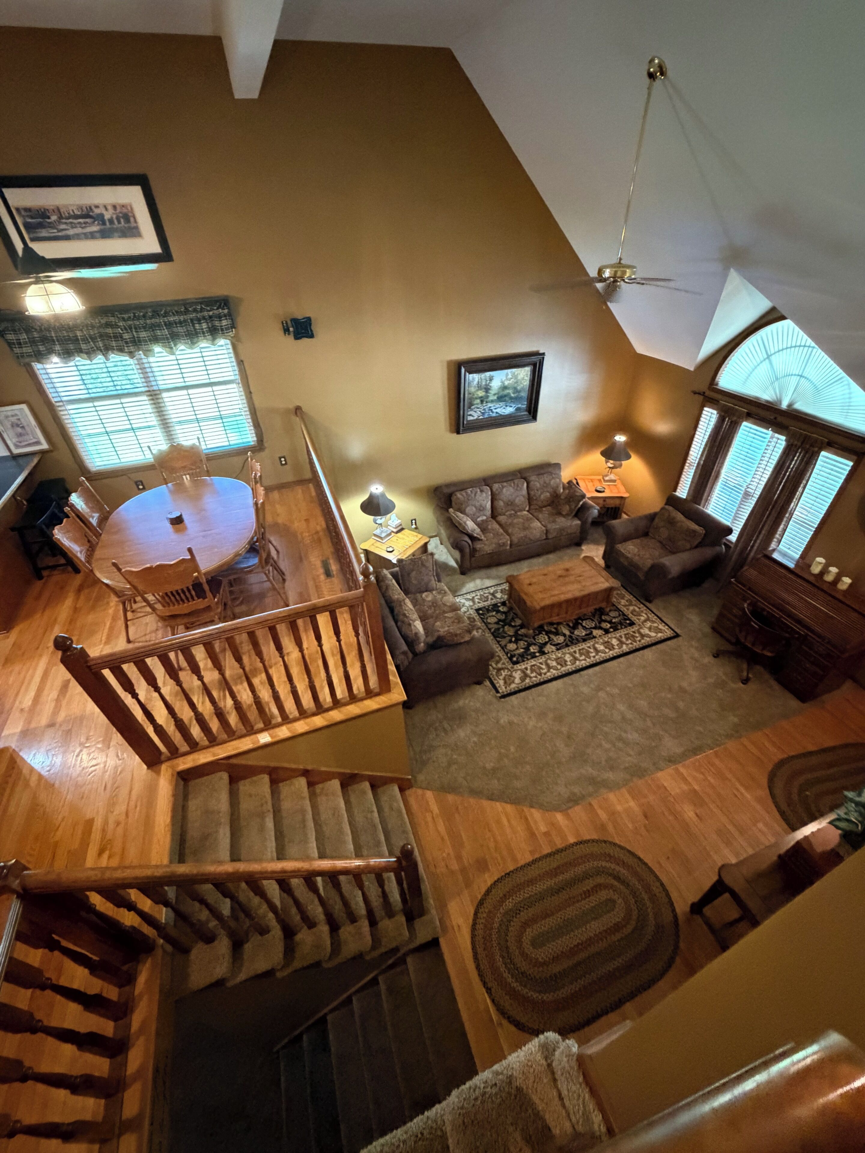 A spacious living area with a wooden dining table, a sofa set, a staircase, and a large window providing natural light.
