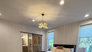Quarto com uma cama grande, um candelabro, uma mesa de cabeceira, uma janela com vista e uma porta que dá para outro cômodo.