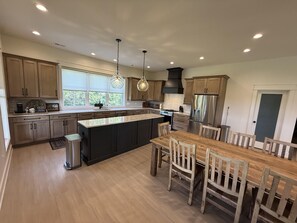 A modern kitchen with a large island, wooden cabinets, stainless steel appliances, and a dining area with a wooden table and chairs.