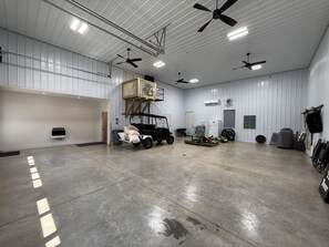 A spacious indoor area with a concrete floor, ceiling fans, and various equipment including a golf cart and a lawnmower.