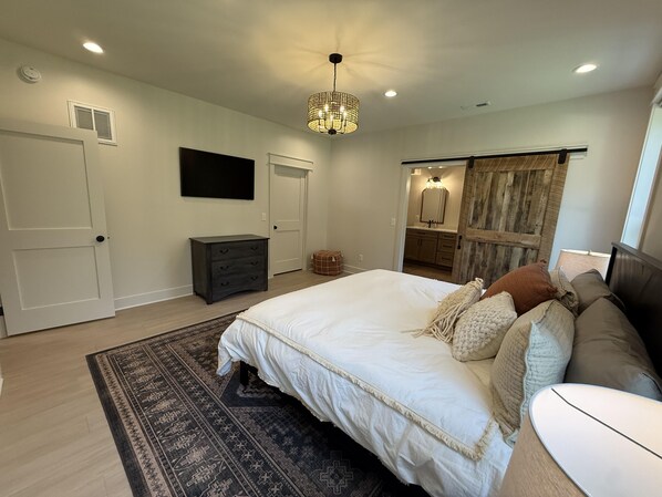 A bedroom with a bed, bedside table, dresser, and a hanging light fixture.