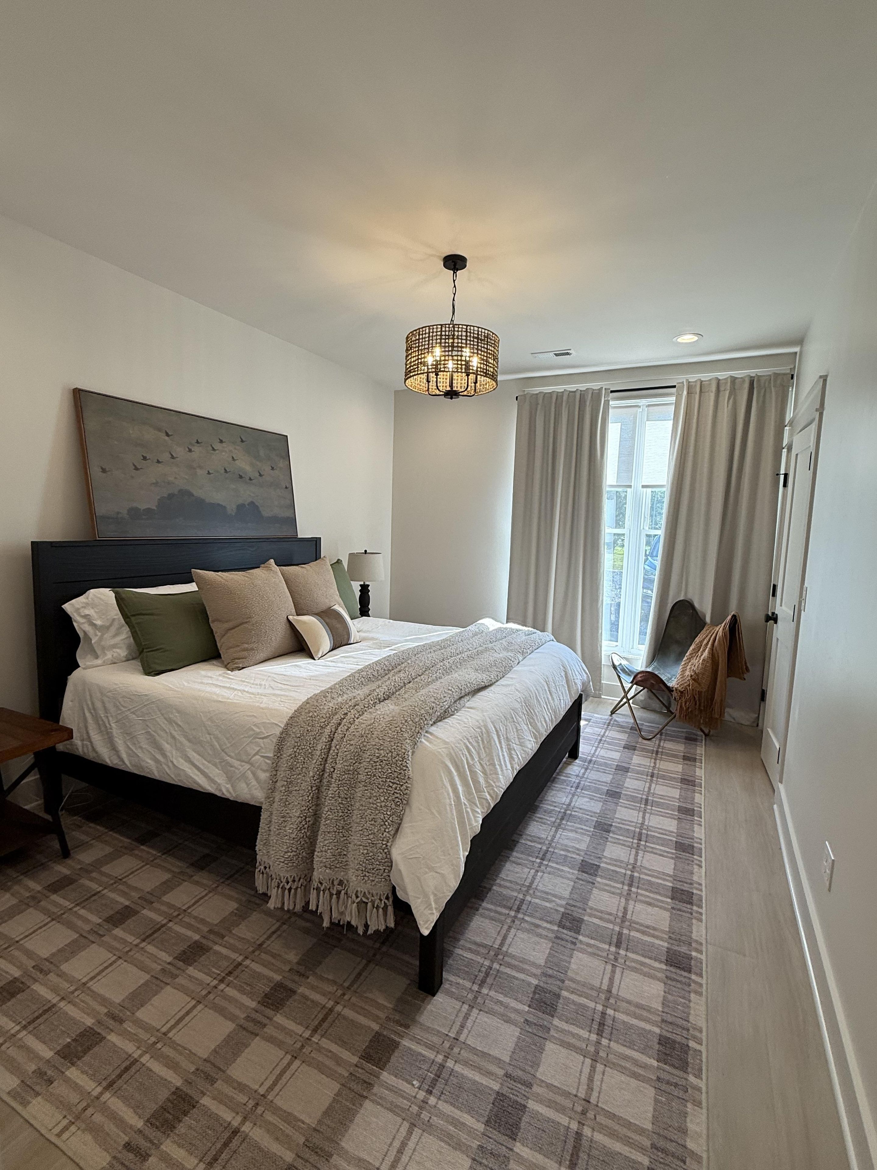 A bedroom with a bed, a chandelier, a painting, and a view of the outdoors.