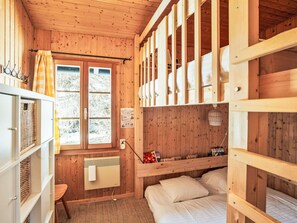Ein Zimmer in einer Holzhütte mit Etagenbetten, einem Fenster, einer Heizung und einem kleinen Tisch.