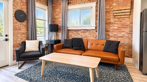 Un salon avec un mur en briques, un canapé, un fauteuil, une table basse et une horloge.