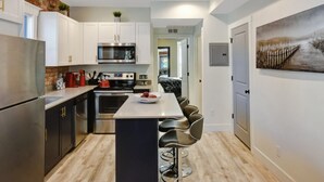 Une cuisine moderne avec des meubles blancs, des appareils en acier inoxydable et un îlot central doté de tabourets de bar.