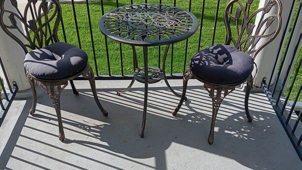 Un balcon avec deux chaises en métal et une petite table ronde, agrémenté d’un motif en forme de grillage métallique.