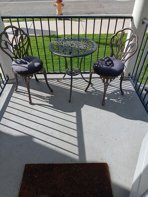 Un balcon avec deux chaises en métal et une petite table ronde, agrémenté d’un motif en forme de grillage métallique.
