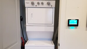 Une petite buanderie équipée d’un lave-linge et d’un sèche-linge à chargement frontal, d’un panneau de commande et d’une porte donnant sur une autre pièce.