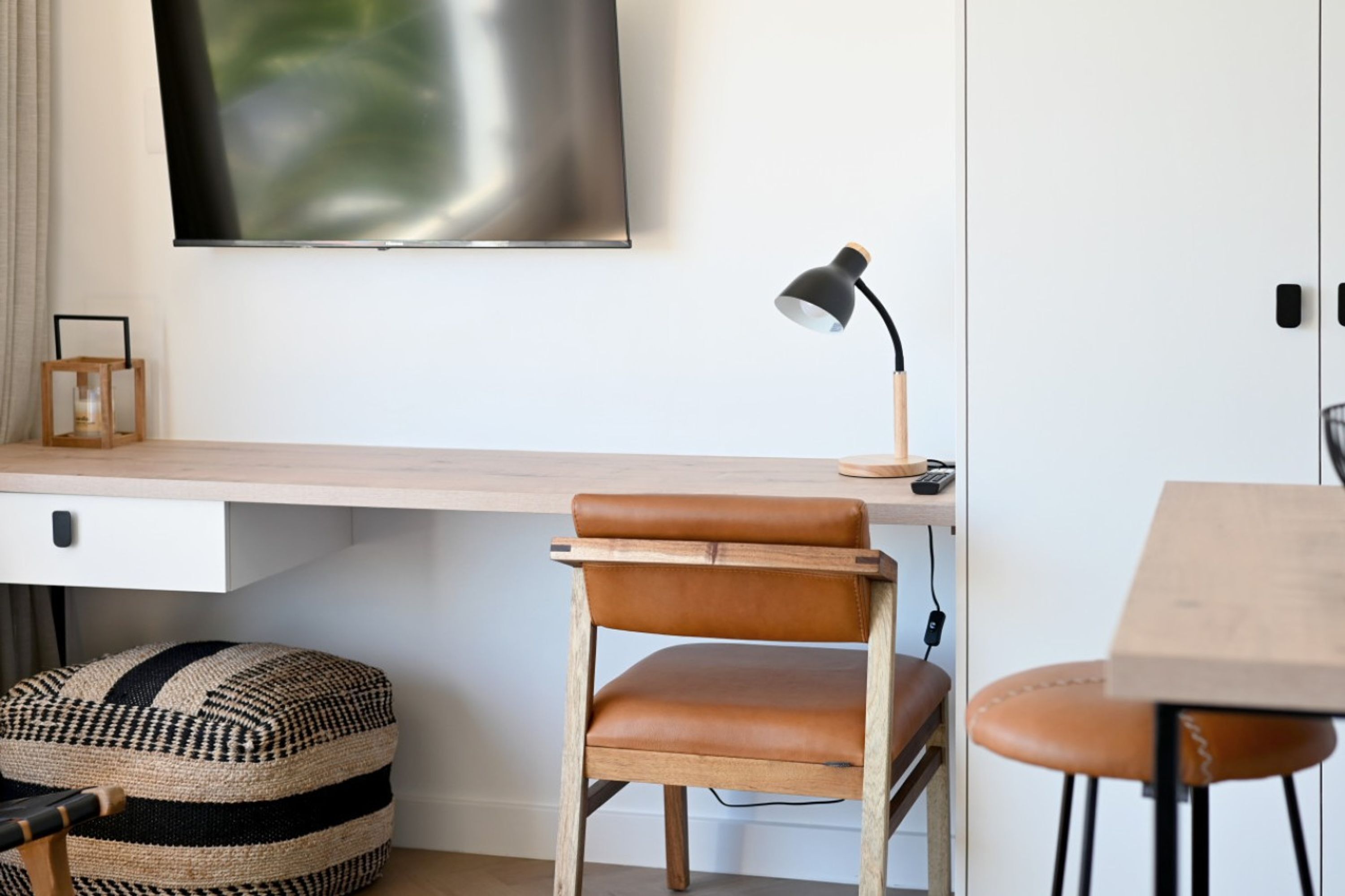 A modern workspace with a wooden desk, leather chair, and a mounted lamp.
