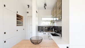 Uma cozinha moderna com armários brancos, uma mesa de jantar de madeira e uma cesta de arame preta.