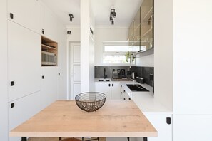 Eine moderne Küche mit weißen Schränken, einem Holztisch und einem schwarzen Drahtkorb.