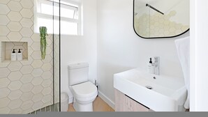 Um banheiro moderno com parede de azulejos hexagonais, vaso sanitário, pia com espelho e janela.