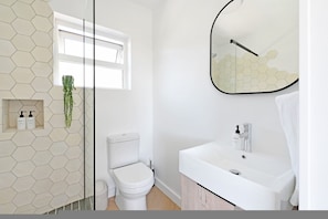 Ein modernes Badezimmer mit Wand aus sechseckigen Fliesen, Toilette, Waschbecken mit Spiegel und einem Fenster.