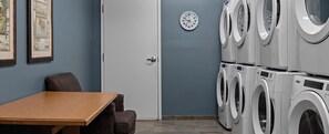 Une buanderie avec des machines à laver superposées, une horloge et des œuvres d’art encadrées accrochées au mur.