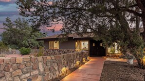 A modern house with a stone wall, a paved driveway, and a well-lit entrance. - West Sedona 3BR retreat with game room, patio, and fenced yard. (Sedona)