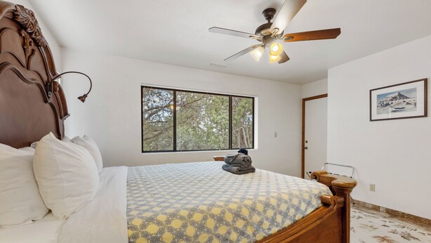 A bedroom with a wooden bed, a ceiling fan, a window with blinds, and a framed picture on the wall. - West Sedona 3BR retreat with game room, patio, and fenced yard. (Sedona)