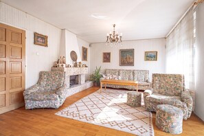Een klassieke woonkamer met een open haard, gestreept meubilair en ingelijste kunstwerken aan de muren.
