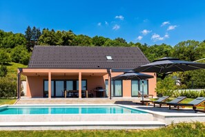Una casa moderna con piscina, mobiliario exterior y patio cubierto.
